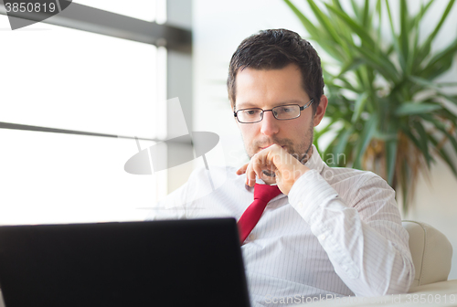 Image of Businessman in office reading on laptop computer.