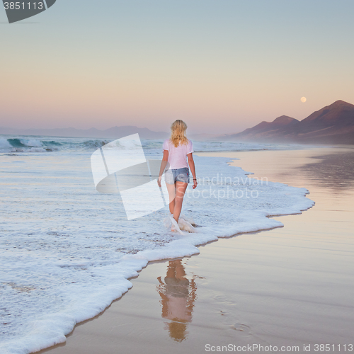 Image of Lady walking on sandy beach in sunset.