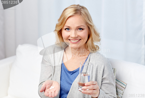 Image of happy woman with medicine and water glass at home