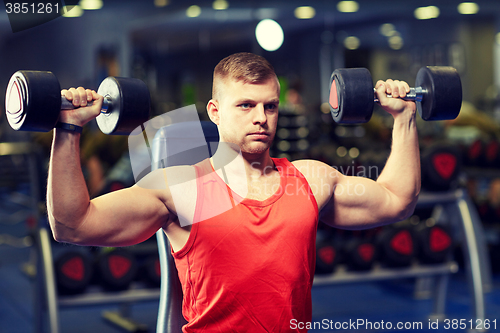 Image of young man with dumbbells flexing muscles in gym