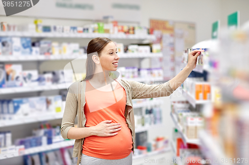 Image of happy pregnant woman choosing medicine at pharmacy