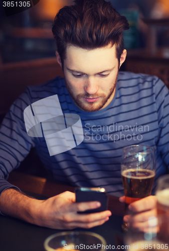 Image of man with smartphone drinking beer at bar