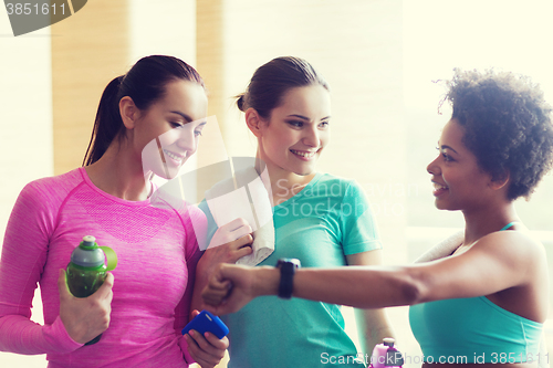 Image of happy women showing time on wrist watch in gym