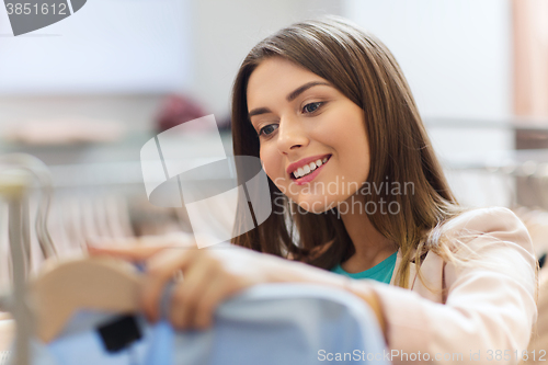 Image of happy young woman choosing clothes in mall