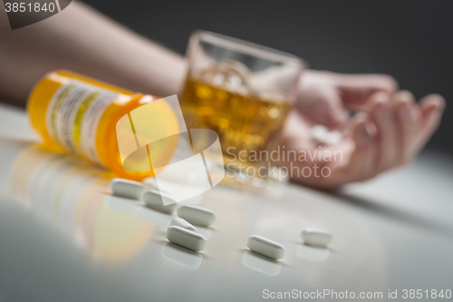 Image of Hand on Ground Behind Scattered Drugs and Glass of Alcohol