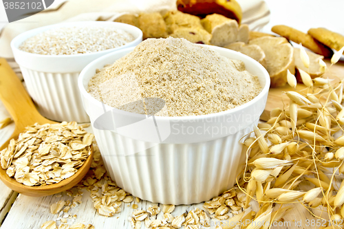 Image of Flour oat in white bowl with flakes in spoon on board