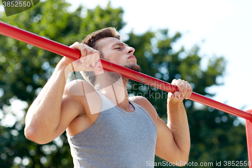 Image of young man exercising on horizontal bar outdoors