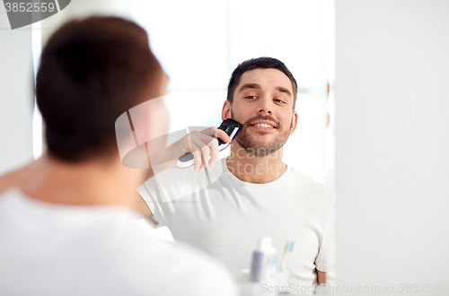 Image of man shaving beard with trimmer at bathroom