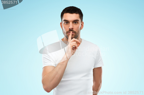 Image of young man making hush sign over blue background