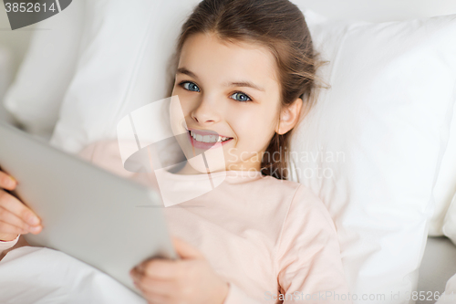 Image of happy girl lying in bed with tablet pc at home