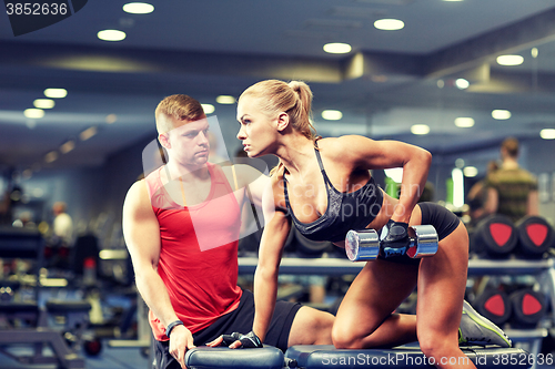 Image of young couple with dumbbell flexing muscles in gym