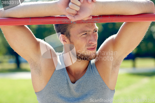 Image of young man exercising on horizontal bar outdoors