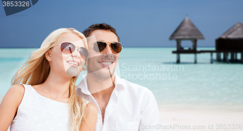 Image of happy couple in shades over beach with bungalow