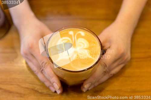 Image of close up of hands with latte art in coffee cup