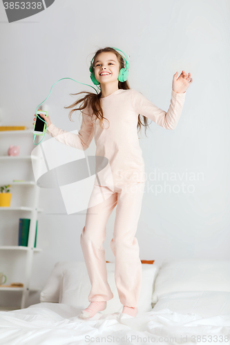 Image of girl jumping on bed with smartphone and headphones