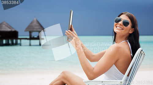 Image of smiling woman with tablet pc sunbathing on beach