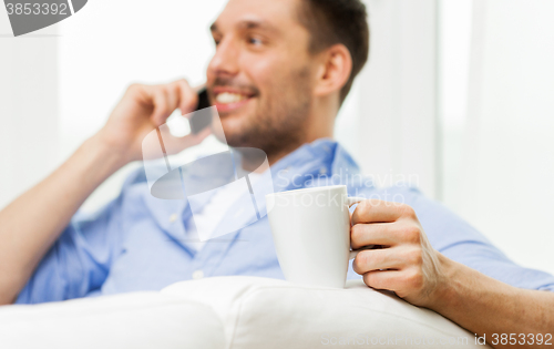 Image of smiling man with cup calling on smartphone at home