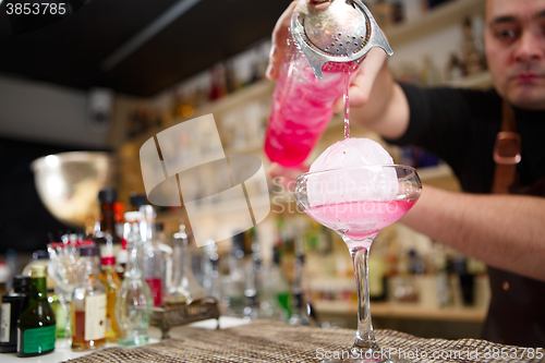 Image of Close-up of bartender hand pouring pink cocktail drink in bar