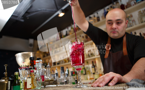 Image of Bartender pouring red cocktail into glass at the bar