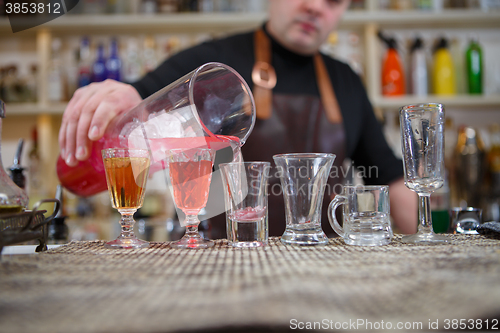 Image of Bartender pours various of alcohol drink into small glasses on bar