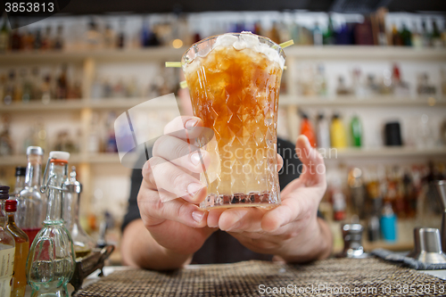 Image of Bartender is standing in pub? holding cocktail and giving glass forward. Focus on beverage.