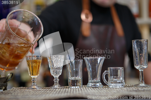 Image of Bartender pours various of alcohol drink into small glasses on bar