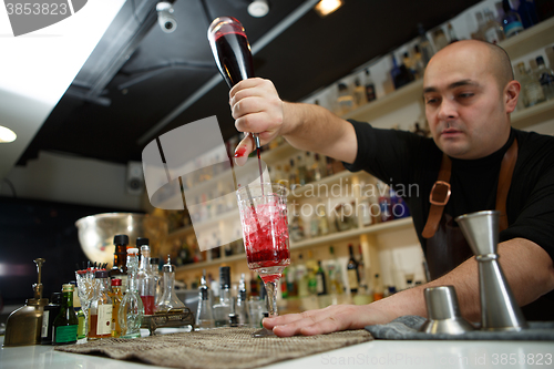 Image of Bartender pouring red cocktail into glass at the bar