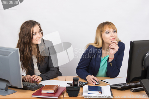 Image of Office worker looking with distaste at the colleague sitting next to staring at a computer monitor