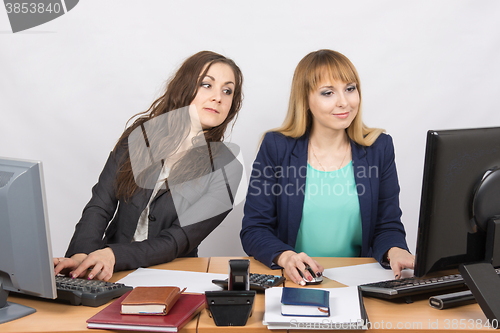 Image of Office worker on the sly looks at the monitor colleague sitting next to a computer