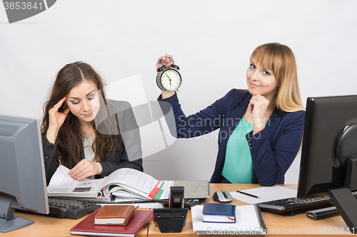 Image of in the office, one employee is looking forward to the end of the day, while the other continues to work intensively