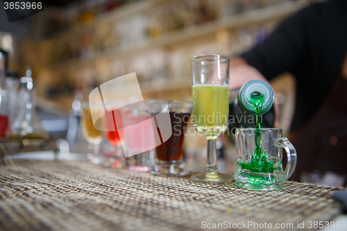 Image of Bartender pours various of alcohol drink into small glasses on bar