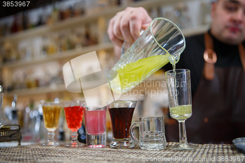 Image of Bartender pours various of alcohol drink into small glasses on bar