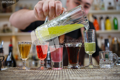 Image of Bartender pours various of alcohol drink into small glasses on bar