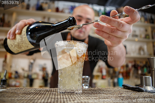 Image of Bartender pouring cocktail into glass at the bar