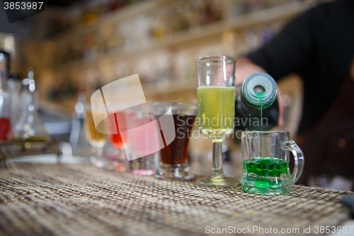 Image of Bartender pours various of alcohol drink into small glasses on bar