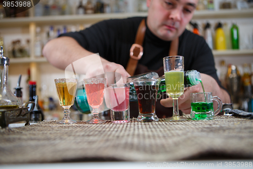 Image of Bartender pours various of alcohol drink into small glasses on bar