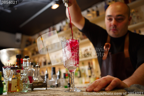 Image of Bartender pouring red cocktail into glass at the bar