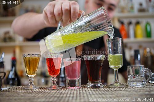 Image of Bartender pours various of alcohol drink into small glasses on bar