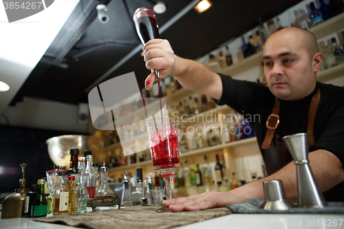 Image of Bartender pouring red cocktail into glass at the bar