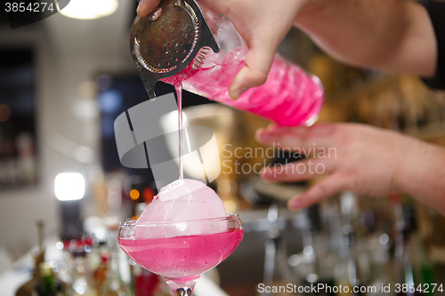 Image of Close-up of bartender hand pouring pink cocktail drink in bar