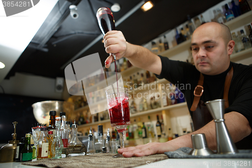 Image of Bartender pouring red cocktail into glass at the bar