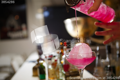 Image of Close-up of bartender hand pouring pink cocktail drink in bar