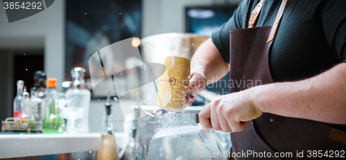 Image of Bartender breaks ice with wooden hammer