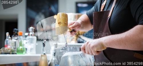 Image of Bartender breaks ice with wooden hammer