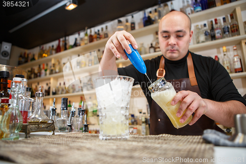 Image of barman using a hand mixer to prepare drink in  bar or pub