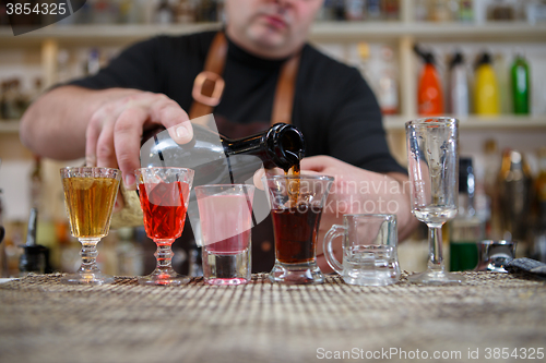 Image of Bartender pours various of alcohol drink into small glasses on bar