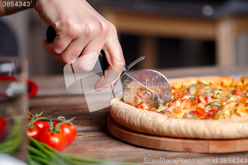 Image of Slicing fresh pizza with roller knife. 