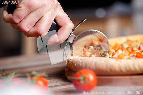 Image of Slicing fresh pizza with roller knife. 