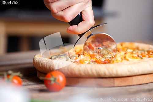 Image of Slicing fresh pizza with roller knife. 