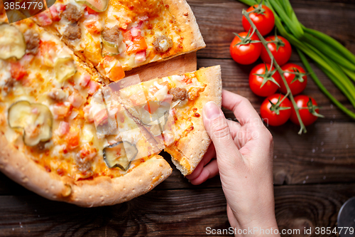 Image of Hand picking tasty slice of pizza lying on wooden table